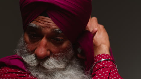 Primer-Plano-De-Una-Toma-De-Estudio-Con-Iluminación-Tenue-De-Un-Hombre-Sikh-Mayor-Con-Barba-Atando-Una-Tela-Para-Un-Turbante-Contra-Un-Fondo-Oscuro-1